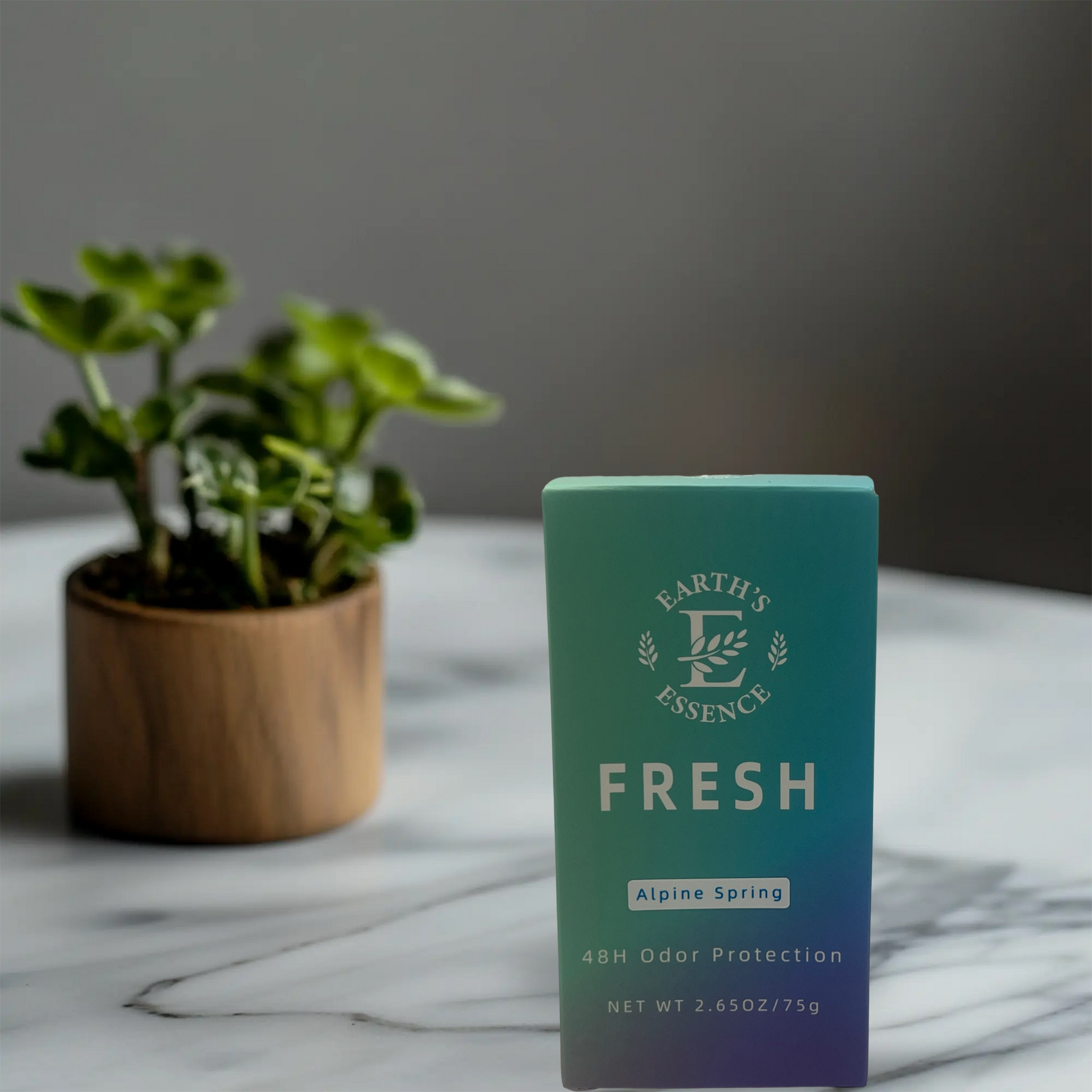 Teal box labeled 'Earth's Essence Fresh' on a marble surface with a plant in the background